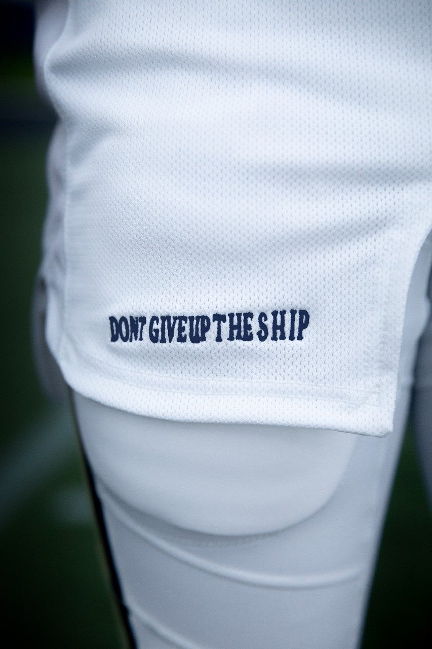 A motto of the United States Navy, "Don't Give Up The Ship," is stitched onto to the lower front side of the jersey.