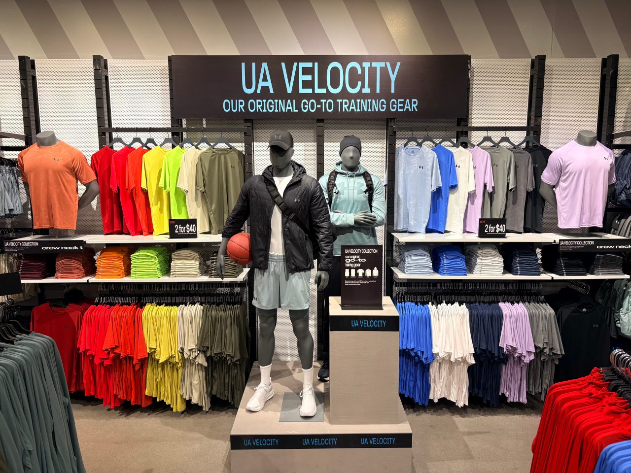 A wall merchandised with "UA Velocity" tees